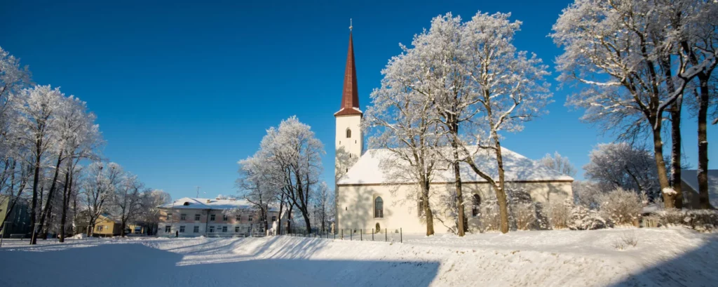 Kirchgebäude umgeben von blätterlosen Bäumen in einer verschneiten Winterlandschaft und bei strahlend blauem Himmel