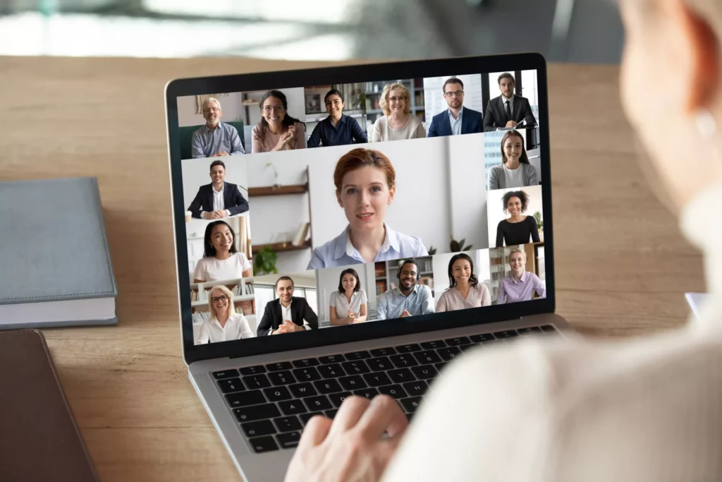 Blick einer Frau auf einen Laptop, auf dem eine geschäftliche Videokonferenz mit einer Vielzahl an Personen zu sehen ist