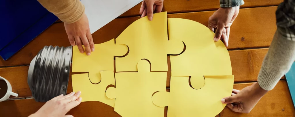 Mehrere Menschen halten Puzzlestücke zusammen, die eine Glühbirne ergeben